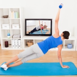 woman watching a workout video in her livingroom and doing a side plank on her yoga mat