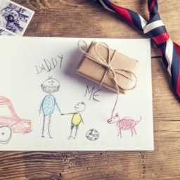 Picture of kids on white paper. Father's tie laying on table and a small wrapped gift.